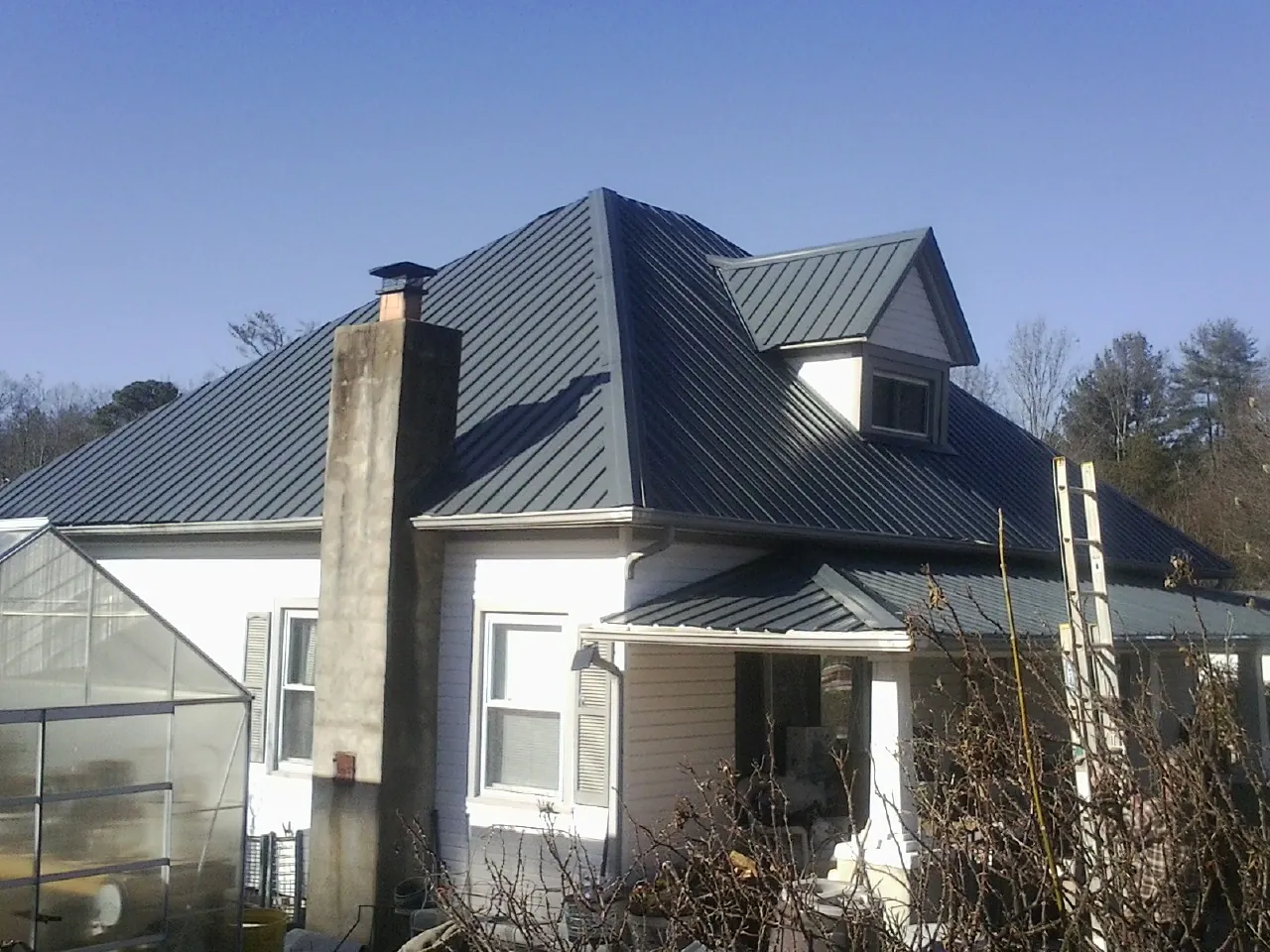 Dark blue standing seam metal roof on a white farmhouse with dormer — Slate & Tile Roof Repair by Roofing Brothers in South Windham