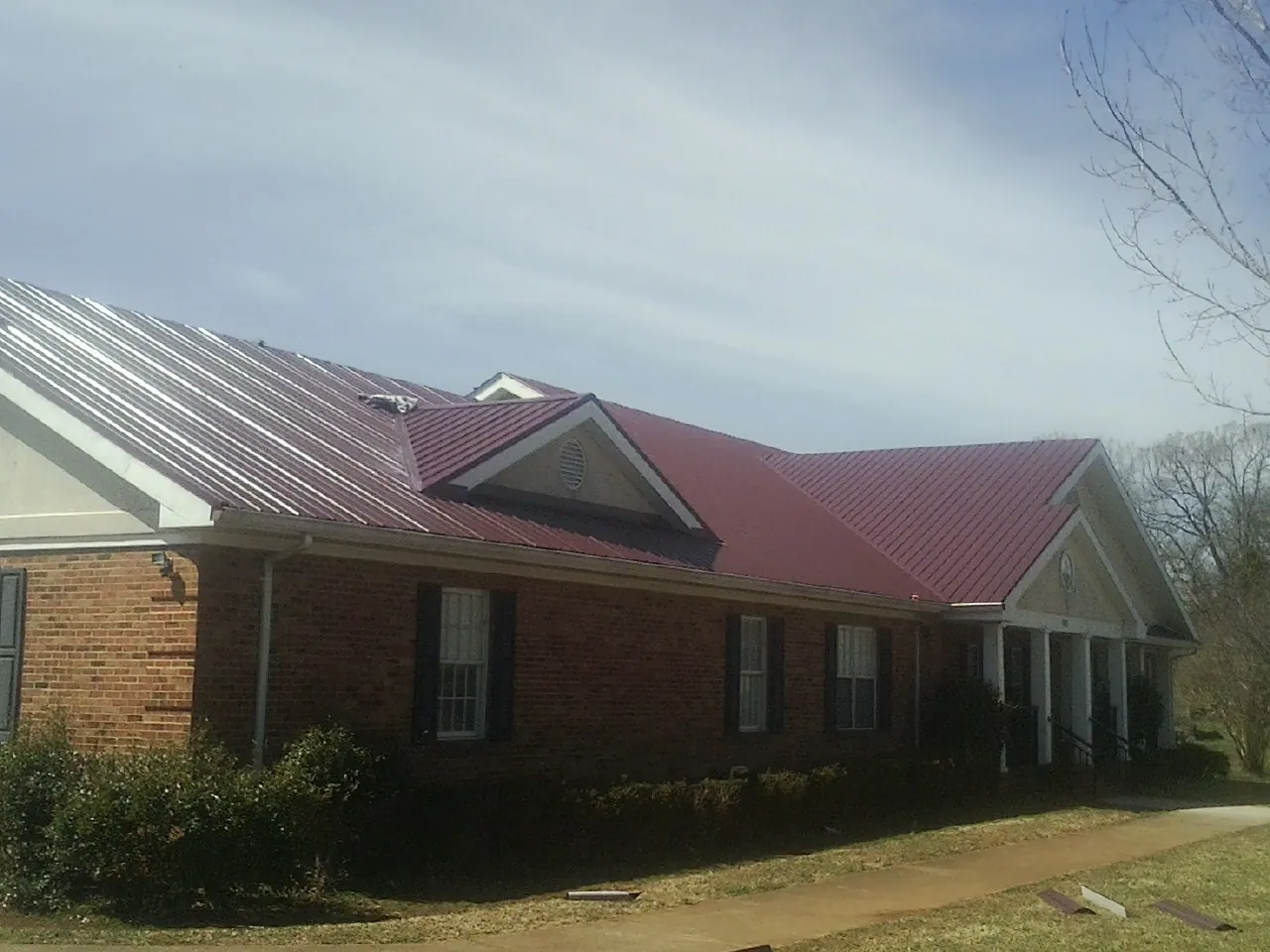 Red metal roof with gabled entries on a long brick building, from a Hail Damage Roof Repair job in South Windham