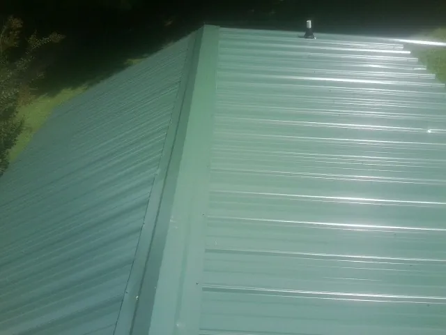 New green metal panels meeting at the ridge of a roof — Flat Roof Repair work by our crew in South Windham