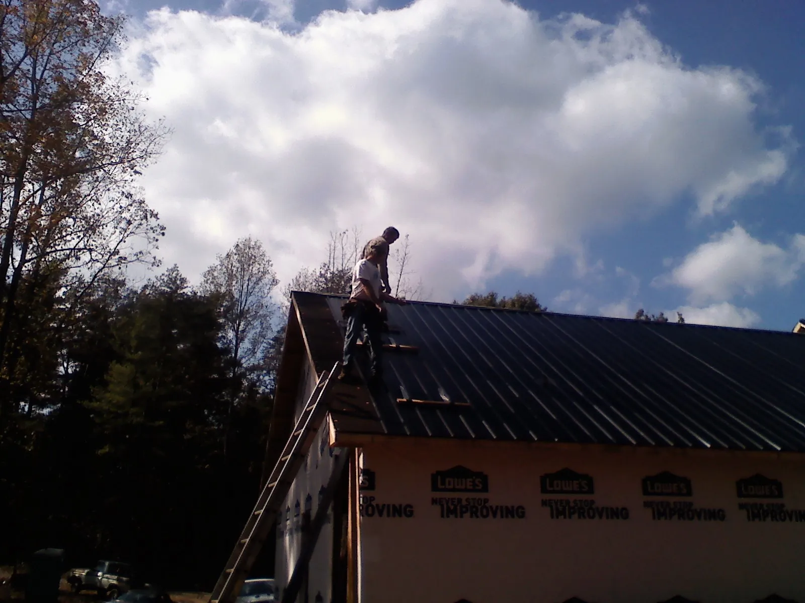 Roofer fastening dark metal panels high against a cloudy sky, from a Roof Inspection job in South Windham