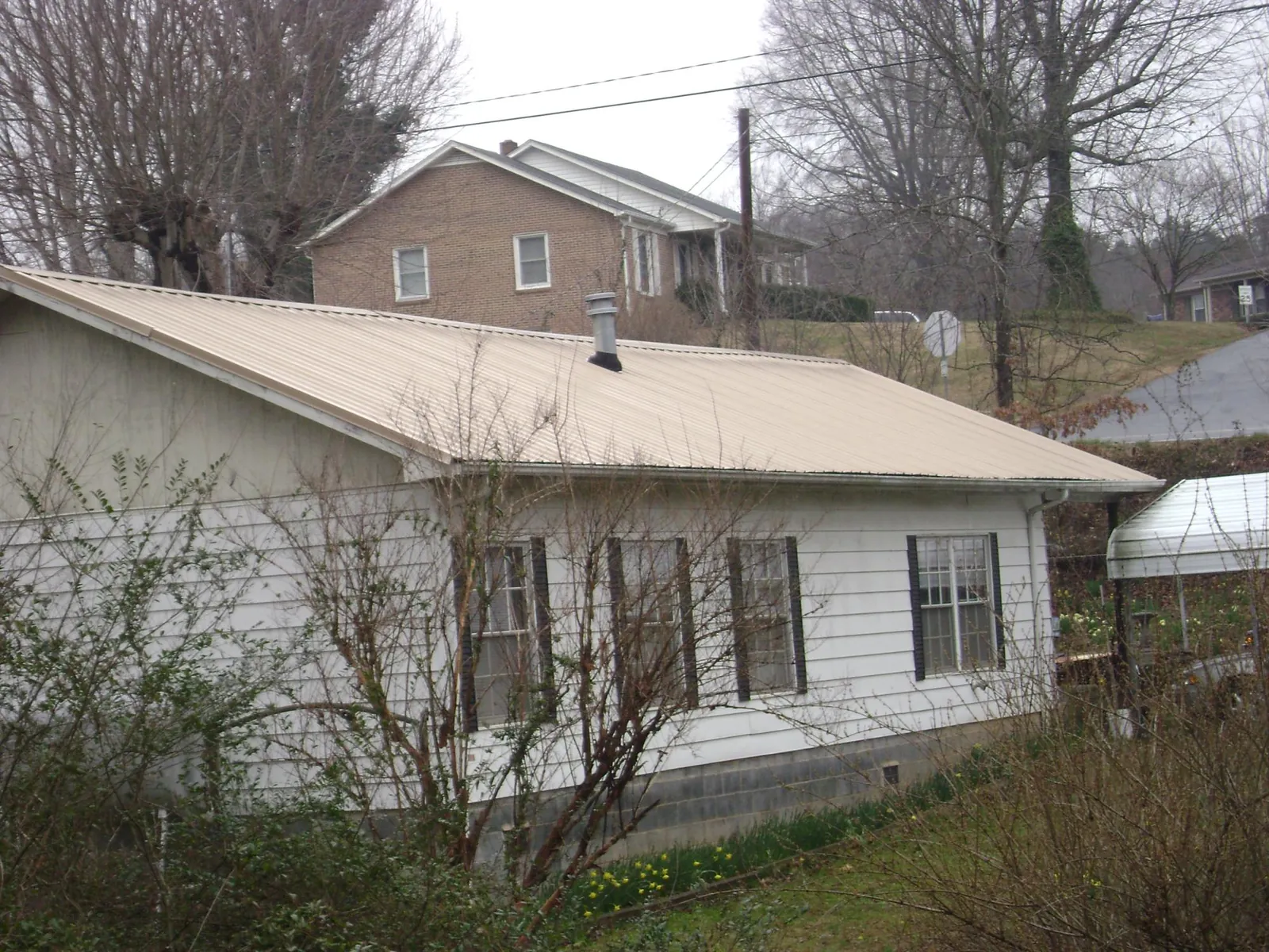 Tan metal roof on a white sided house set into a hillside — Commercial Roofing by Roofing Brothers in South Windham
